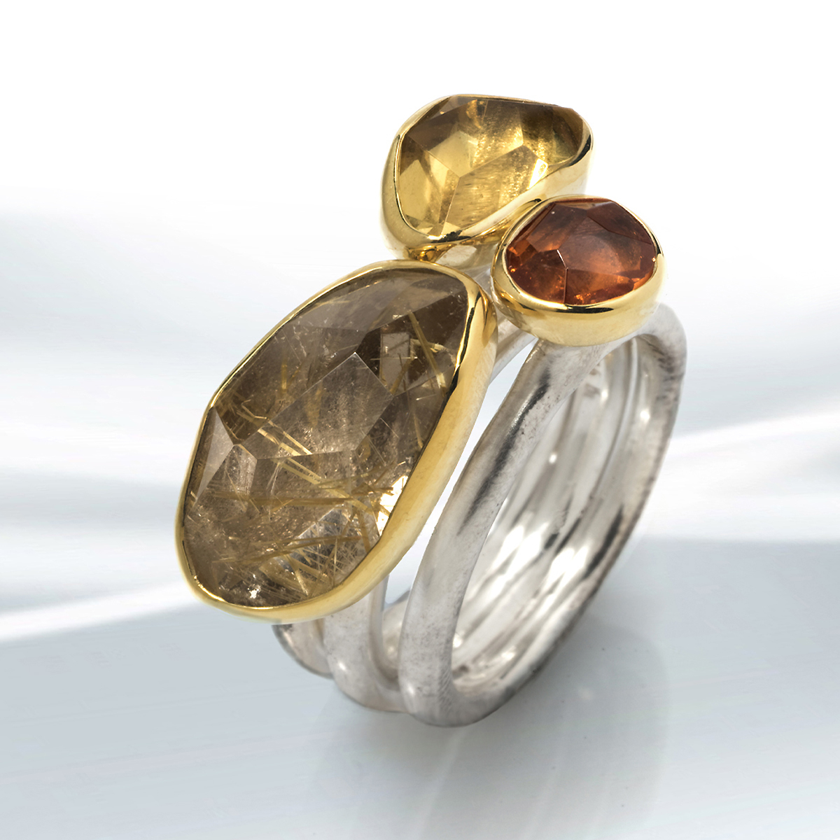 Silver and gold are harmoniously combined with the three impressive stones in this triple band ring which features a rutile quartz, an heliodor and an orange garnet. The stones weight 17,7ct and are all set in a 750 gold bezel.